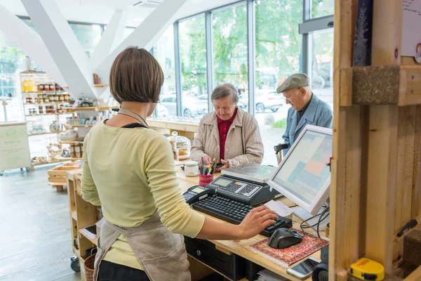 Elderly couple at cashier desk paying to teller in local zero waste store.