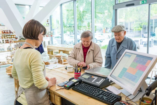 Elderly couple at cashier desk paying to teller in local zero waste store.