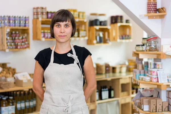 Cherfull young female shop owner posing in front of shelves full of healthy products.