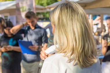 Kadın açık havada canlı seyirci önünde bir konuşma yapıyor.