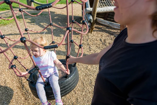 Mãe balançando seu bonito jovem filha no parque infantil ao ar livre . — Fotografia de Stock