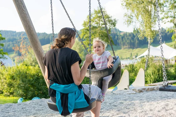 Mãe e filha balançando em um playground no parque local . — Fotografia de Stock