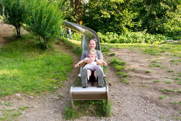 Padre e figlia a cavallo di un lungo scivolo al parco locale . — Foto Stock