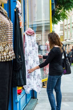 Çekici esmer, açık hava butik dükkanında tasarımcı kıyafetlerine bakıyor..