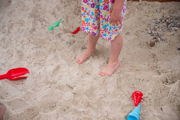 Visão suspensa de brinquedos de areia na praia com pés de criança de pé perto . — Fotografia de Stock