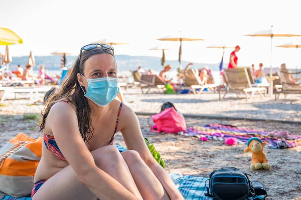 Młoda kobieta w masce medycznej siedząca na plaży. Nowa koncepcja normalna. — Zdjęcie stockowe