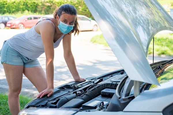 Woman wearing medical mask trying to fix broken car engine. — Stock Photo, Image