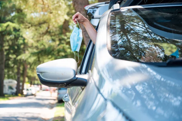 Woman stretching her arm through a car window while holding a medical mask. — Stock Photo, Image