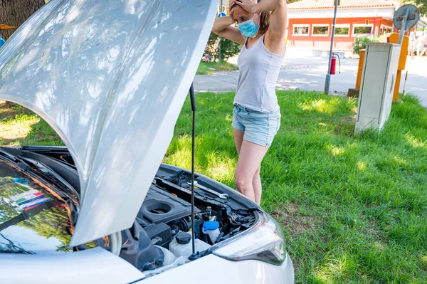Woman wearing medical mask trying to fix broken car engine. — Stock Photo, Image