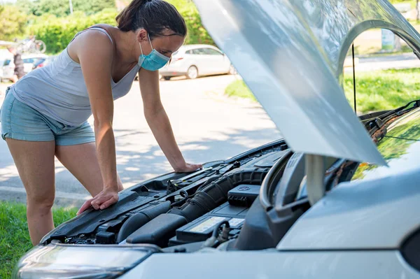 Woman wearing medical mask trying to fix broken car engine. — Stock Photo, Image