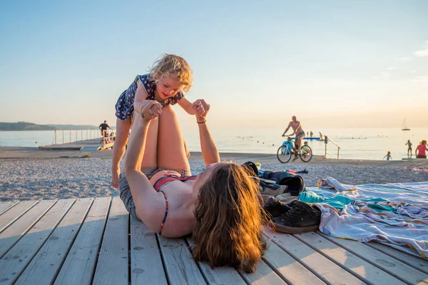 Jovem mãe usando máscara médica brincando com sua filha na praia. Novo conceito normal . — Fotografia de Stock