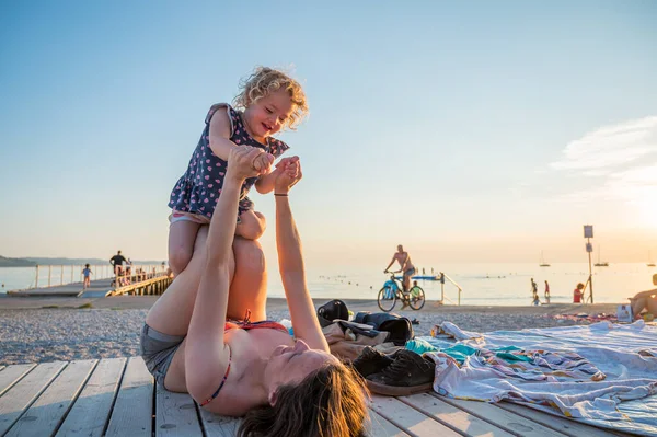 Jovem mãe usando máscara médica brincando com sua filha na praia. Novo conceito normal . — Fotografia de Stock