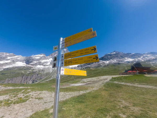 Cervinia, İtalya - 12 Temmuz 2020: Cervinia üzerinde farklı dağ rotalarında rehberlik eden yürüyüşçülerin bulunduğu sarı tabela direği