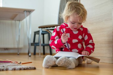 Yerde oturan ve defterine resim çizen tatlı kız..