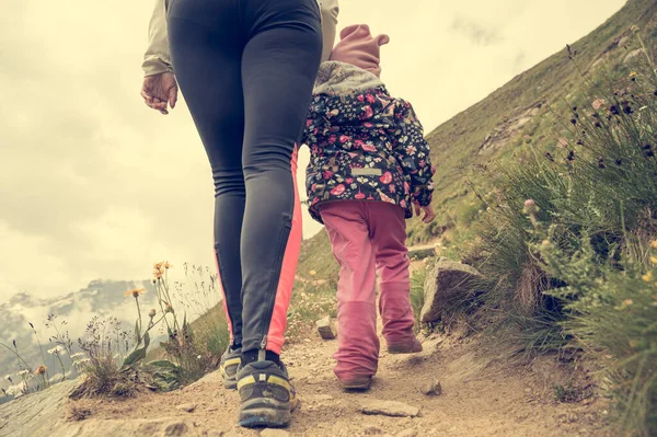 Mother and daughter hiking hand in hand a trail through mountain pastures. — Stock Photo, Image
