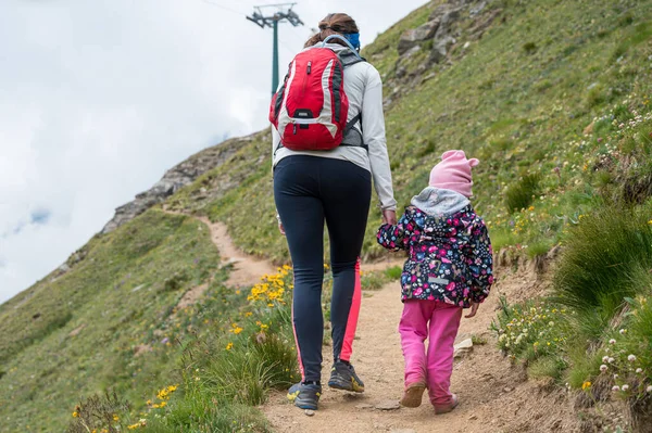 Mãe e filha caminhadas de mãos dadas uma trilha através de pastagens de montanha. — Fotografia de Stock