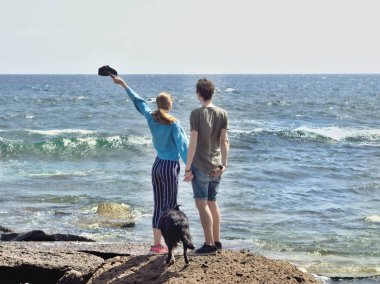 Genç ve sevgi dolu bir çift su kenarında denize bakan yüzleri ile duruyor.