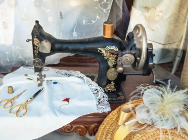 Dekorlu siyah çok eski bir pedal dikiş makinesi, dikiş gereçleri ile çevrili,