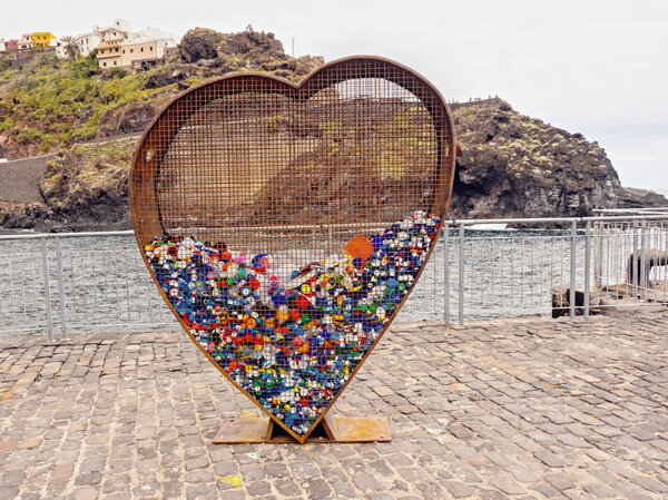 A large rusty, transparent metal heart as a recycling container of plastic closures   