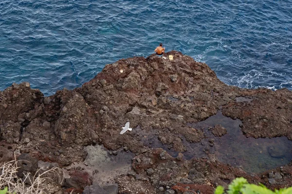 Poruszający się niebieski Ocean Atlantycki i skały wulkaniczne, samotny wędkarz siedzi na skraju skały — Zdjęcie stockowe