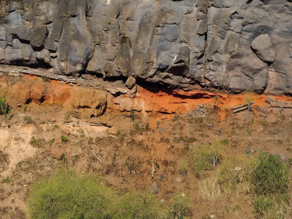 black volcanic ashlar rock and iron-containing red stone layers under it