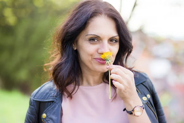 Beautiful middle-age woman in black leather jacket smelling daisy flower. — Stockfoto