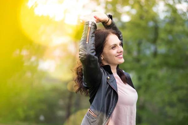 Beautiful, powerful middle-age woman in black leather jacket, arms above head.