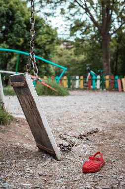 Zincirle kumda yatan kırmızı çocuk sandalet ile parkta kırık salıncak.