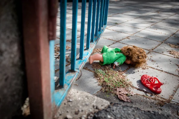 Old doll toy and red sandal thrown on the ground by the blue gate. — Stock Photo, Image