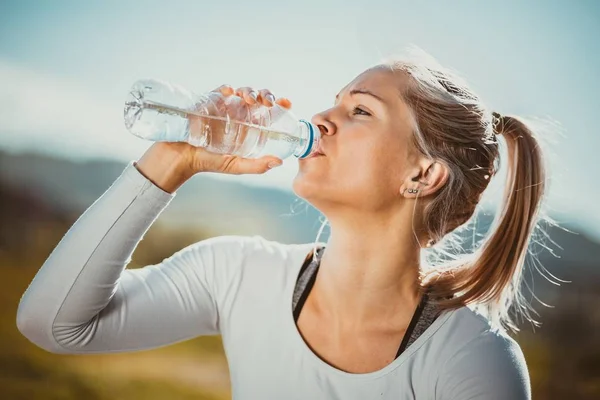 Blonde, powerful fit, sporty woman drinking water after her training