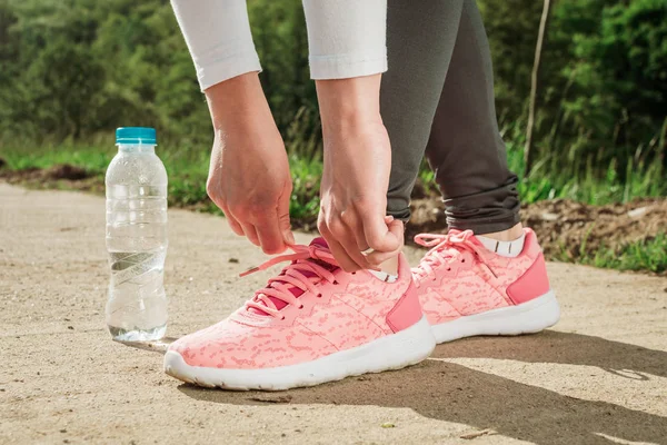 Meisje binden schoenveters op haar roze hardloopschoenen. Water fles naast haar — Stockfoto