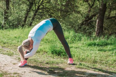 Sarışın kız doğada açık havada pratik yapıyor. Çim alanı. Yan esneme. Fitness, sağlıklı yaşam tarzı