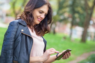 Beautiful middle-age woman in black leather jacket checking her phone.