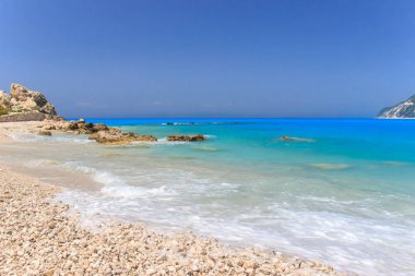 Arka planda mavi gökyüzü ile siyan mavi su ve kaya ile Lefkada Beach