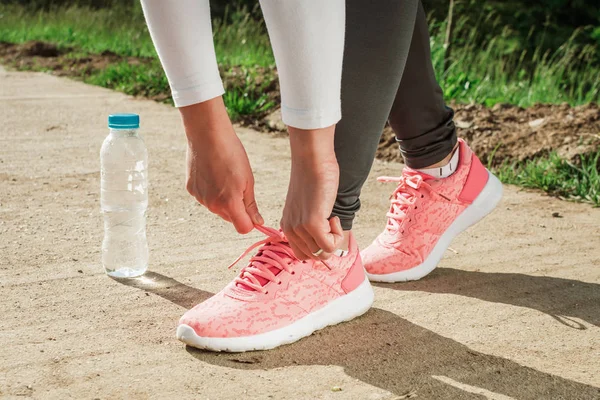 Meisje binden schoenveters op haar hardloopschoenen. Water fles op de grond. — Stockfoto