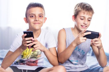 Sevimli küçük çocuklar, kardeşler akıllı telefonlarında oyun oynuyor.