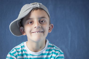 Beysbol şapkası takan sevimli küçük bir öğrencinin yakın çekim portresi. Mavi arka plan