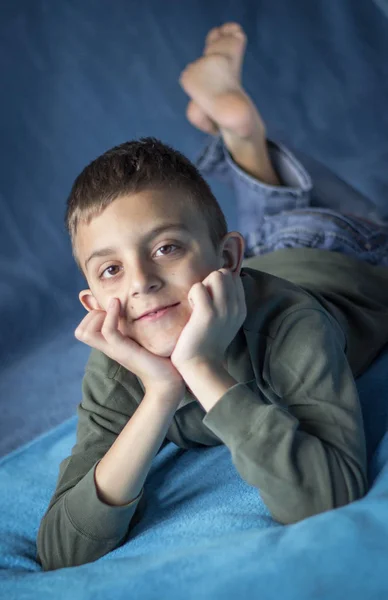 Porträtt av Lille pojke leende, hålla huvudet i händerna, liggande på sängen — Stockfoto