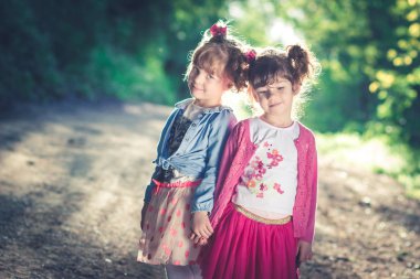 İki küçük kız, pembe elbiseli kız kardeşler, domuz kuyrukları, el ele tutuşan.