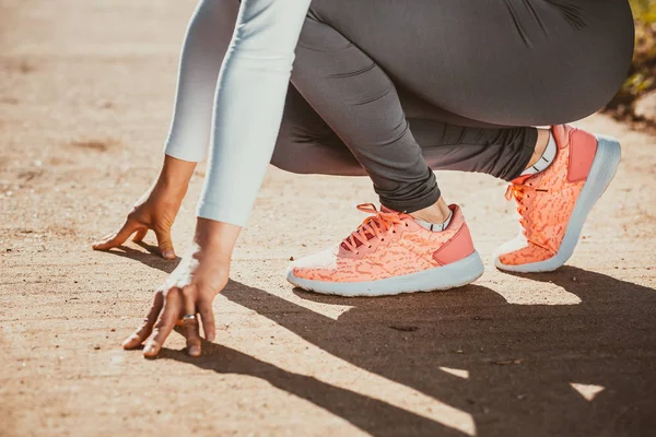 Photo of fit girl with pink sneakers in start position for running.