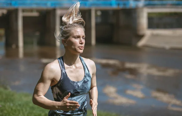 Blonde girl wearing sportswear running in the nature, by the river — Stock Photo, Image