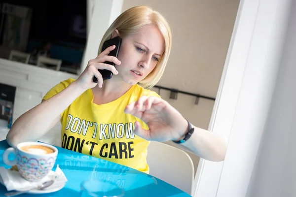 Menina em camiseta amarela olhando para o relógio de pulso enquanto fala no telefone . — Fotografia de Stock