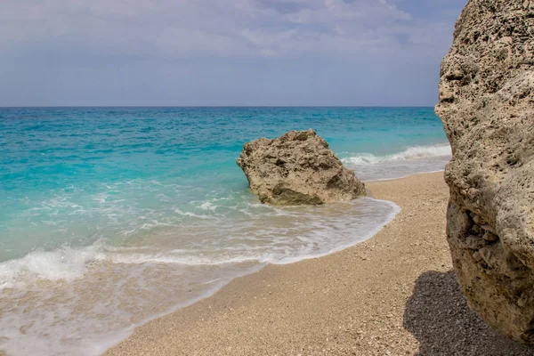 Пляж с голубой голубой водой и скалой на фоне голубого неба — стоковое фото