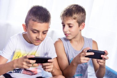 Sevimli, küçük çocuklar, kardeşler akıllı telefonlarında online oyun oynuyor.