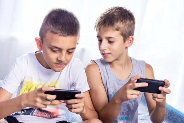 Carino, bambini, fratelli che giocano giochi online sui loro smartphone . — Foto Stock