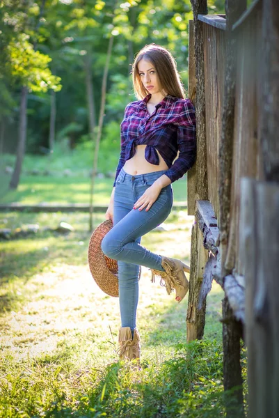 Vaqueira de jeans e camisa quadriculada em pé junto à parede de madeira — Fotografia de Stock