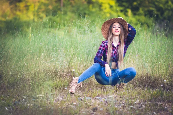 Cowgirl in jeans and checkered shirt posing in provocative pose in the nature — Stock Photo, Image