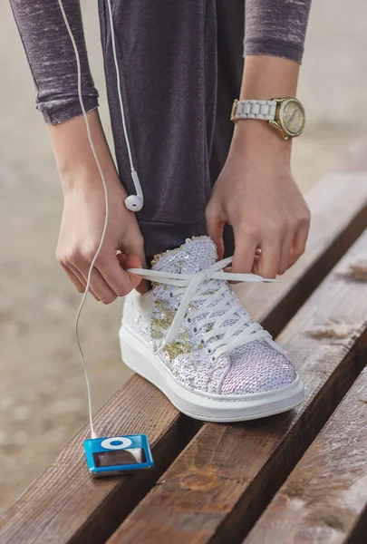Chica atando cordones de zapatos en sus zapatillas blancas modernas en el banco —  Fotos de Stock