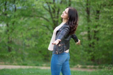 Siyah deri ceketli orta yaşlı kadın geniş, kolları tamamen açık gülümseyen.