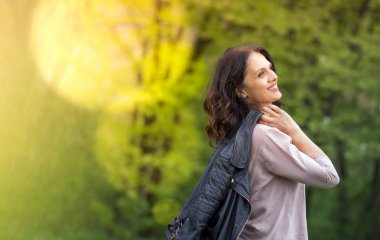Orta yaşlı kadın gülümseyerek, ceketini omzuna dayadı